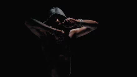 Playboi Carti striking a pose in low light, set against a dark background, captured in a 4K Ultra HD music-themed desktop wallpaper.