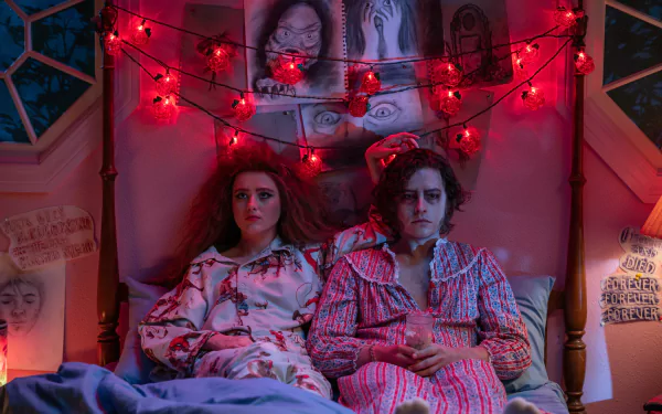A scene from *Lisa Frankenstein*, featuring two characters in pajamas sitting together in a cozy bedroom adorned with red fairy lights, creating an intriguing atmosphere.