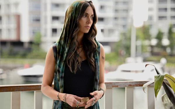 HD desktop wallpaper from the TV Show Apples Never Fall featuring a contemplative woman on a balcony overlooking a marina.