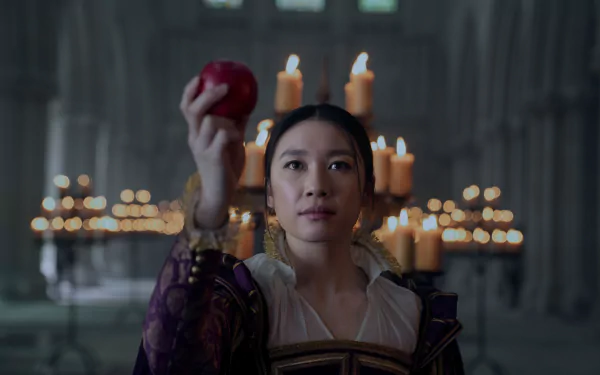 A scene from the TV show 3 Body Problem, featuring a woman holding an apple in a dimly lit setting surrounded by candles, serves as an engaging HD desktop wallpaper.