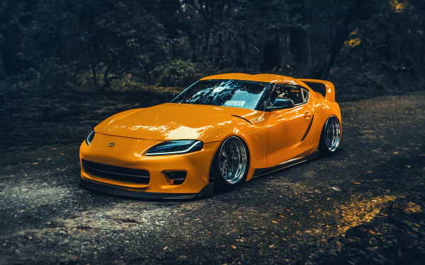A striking orange Toyota Supra A90 parked on a winding road, surrounded by lush greenery, capturing the essence of speed and style in this HD desktop wallpaper.