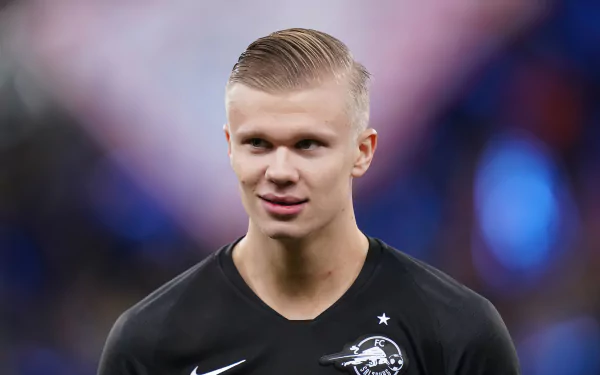 Professional soccer player in a black sports kit against a blurred stadium background, featured in a high-definition desktop wallpaper.