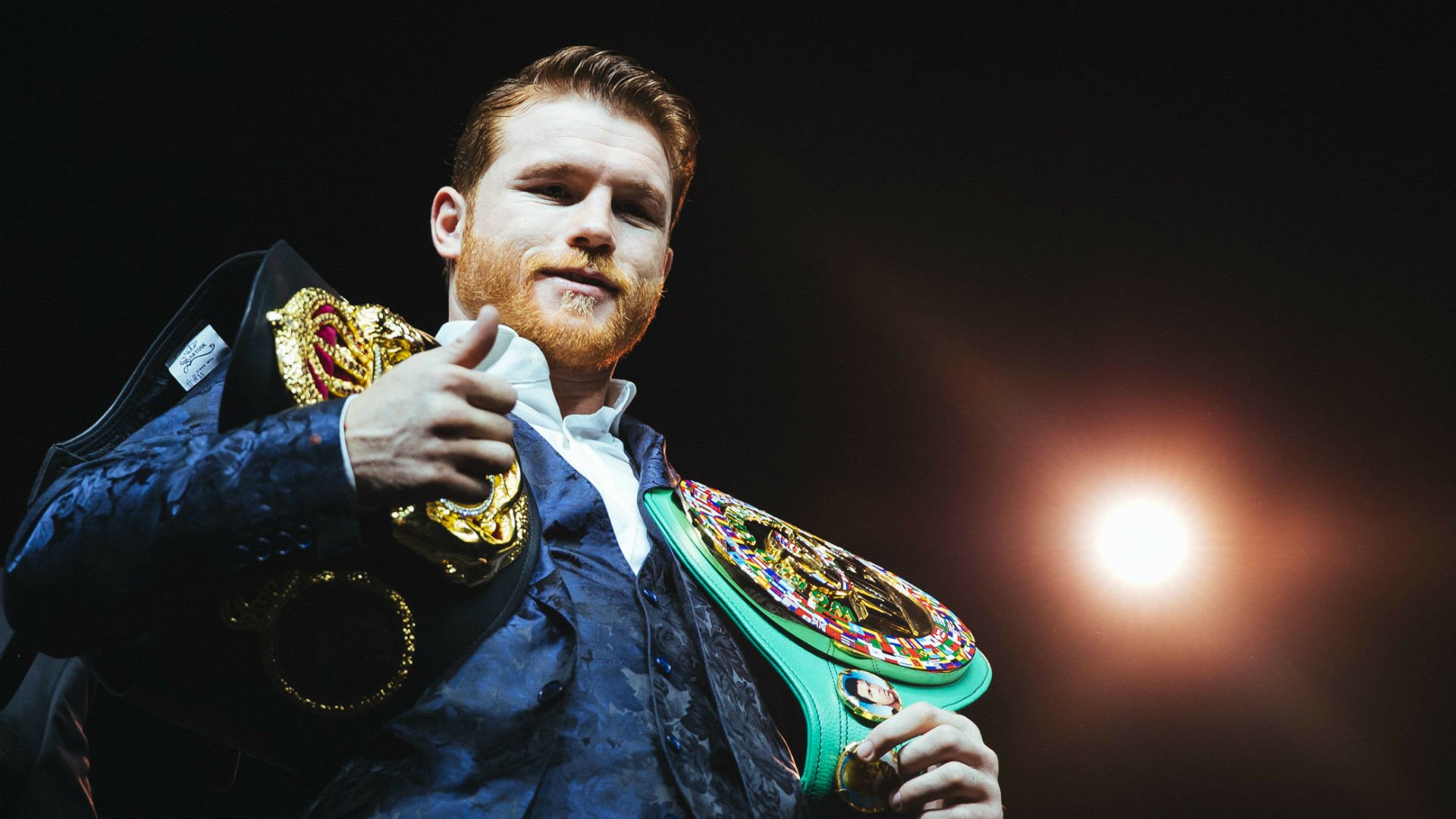 HD desktop wallpaper of a boxer in the ring, confidently holding championship belts with a spotlight in the background.