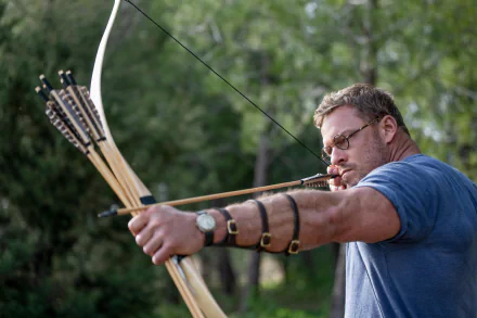 A man focused on aiming a bow and arrow in an outdoor setting, potentially representing a scene related to 'The Ministry of Ungentlemanly Warfare' as part of a high-definition desktop wallpaper.
