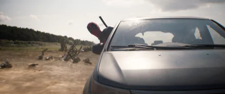 HD desktop wallpaper featuring Deadpool peeking out from the roof of a car in a dusty landscape, evoking a scene from a Deadpool & Wolverine movie.
