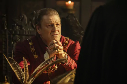 HD desktop wallpaper from the TV show Shardlake featuring a character in a richly decorated room, dressed in a red, regal costume, intently listening to someone out of frame.