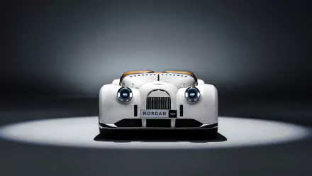 HD desktop wallpaper featuring the front view of a white Morgan Midsummer car, illuminated in a spotlight against a dark background.