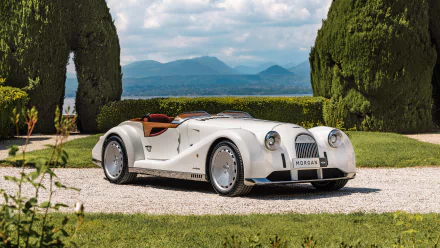 A stunning HD desktop wallpaper featuring a classic white Morgan Midsummer car, set against a picturesque background with lush greenery and distant mountains.