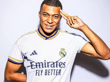 HD desktop wallpaper featuring Kylian Mbappé in a Real Madrid C.F. jersey, smiling and making a salute gesture against a plain white background. Tags: Sports, soccer, Real Madrid C.F., Kylian Mbappé.