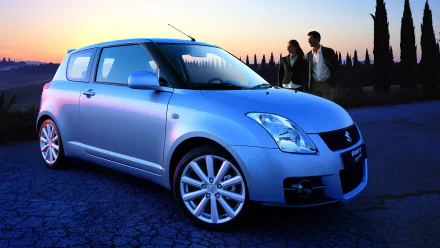 HD wallpaper showcasing a Suzuki Swift Sport car at sunset, with a couple in the background and a scenic landscape featuring tall trees.