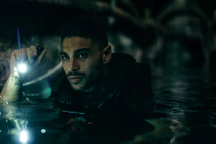 HD desktop wallpaper of a scene from the movie Under Paris, featuring a man illuminated by a flashlight, partially submerged in water against a dark atmospheric backdrop.