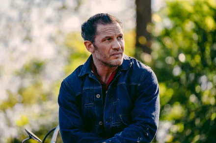 HD desktop wallpaper from the movie The Bikeriders, featuring Tom Hardy in a denim jacket, set against a natural blurred background.