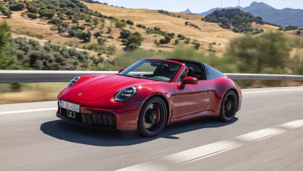 HD desktop wallpaper featuring a red Porsche 911 Targa 4 GTS driving on a scenic road with rolling hills and trees in the background.
