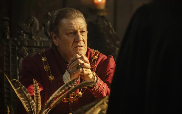 HD desktop wallpaper from the TV show Shardlake featuring a character in a richly decorated room, dressed in a red, regal costume, intently listening to someone out of frame.
