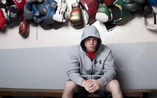 HD desktop wallpaper featuring a boxer in a hoodie seated under a collection of various hanging boxing gloves.