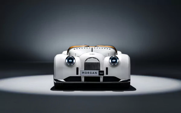 HD desktop wallpaper featuring the front view of a white Morgan Midsummer car, illuminated in a spotlight against a dark background.