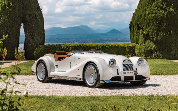 A stunning HD desktop wallpaper featuring a classic white Morgan Midsummer car, set against a picturesque background with lush greenery and distant mountains.