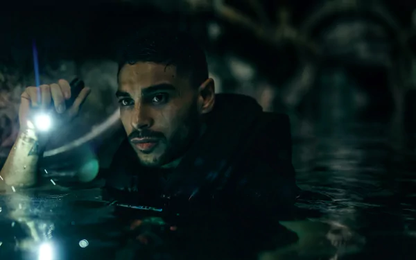 HD desktop wallpaper of a scene from the movie Under Paris, featuring a man illuminated by a flashlight, partially submerged in water against a dark atmospheric backdrop.