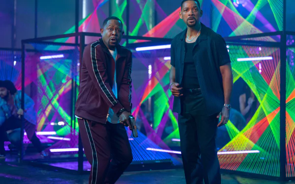 A vibrant HD desktop wallpaper featuring Will Smith and Martin Lawrence in a scene from the movie Bad Boys: Ride or Die, against a backdrop of colorful neon lights.