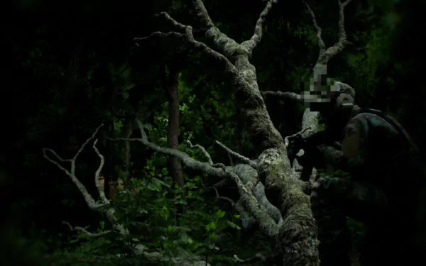 A high-definition bodycam-style desktop wallpaper showing a soldier in a dark, dense forest, partially obscured by a tree. The scene exudes a tense, stealthy atmosphere.