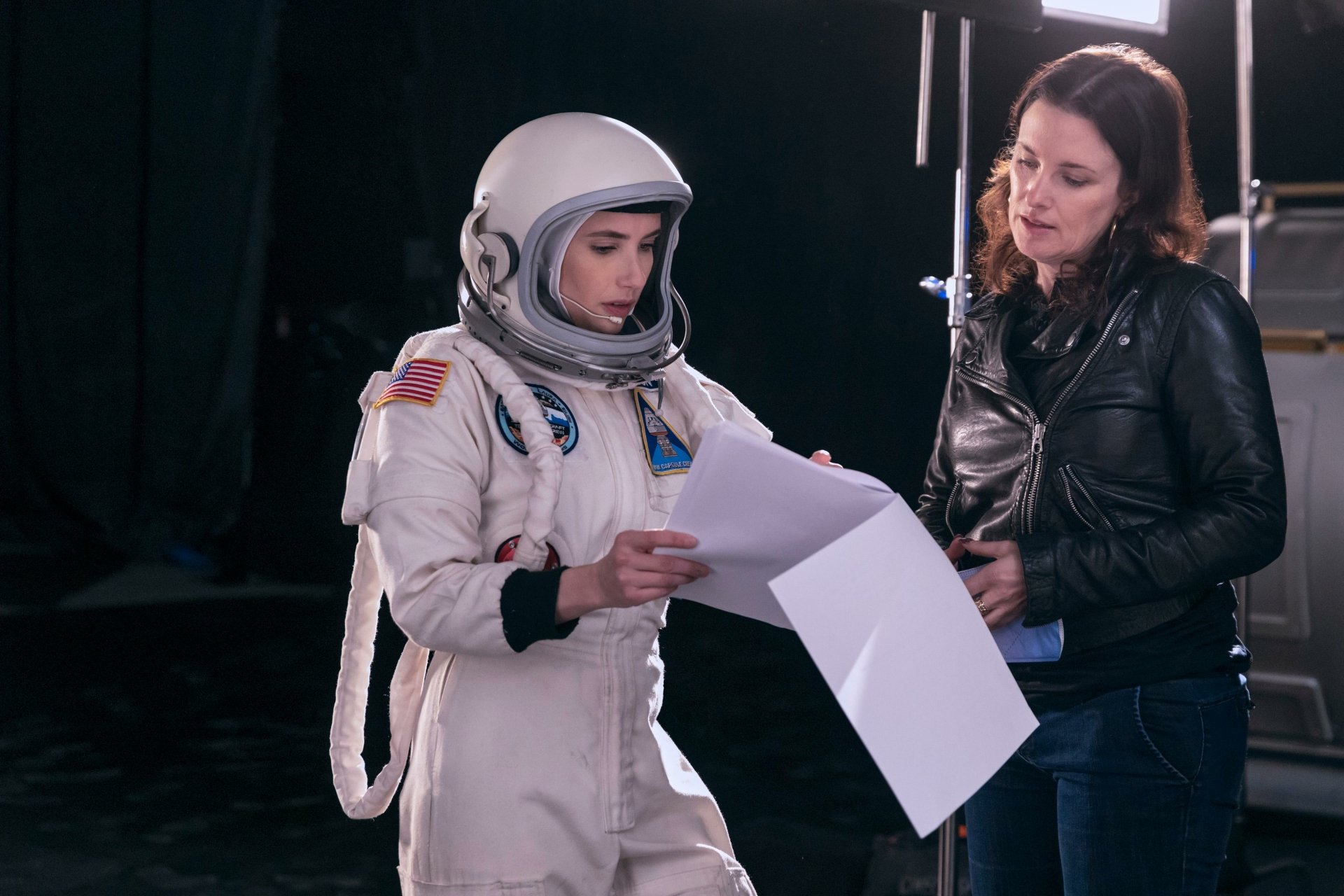 A scene from the movie Space Cadet, featuring an actress in a spacesuit reviewing a script with a director, set against a backdrop of a film studio. HD desktop wallpaper.