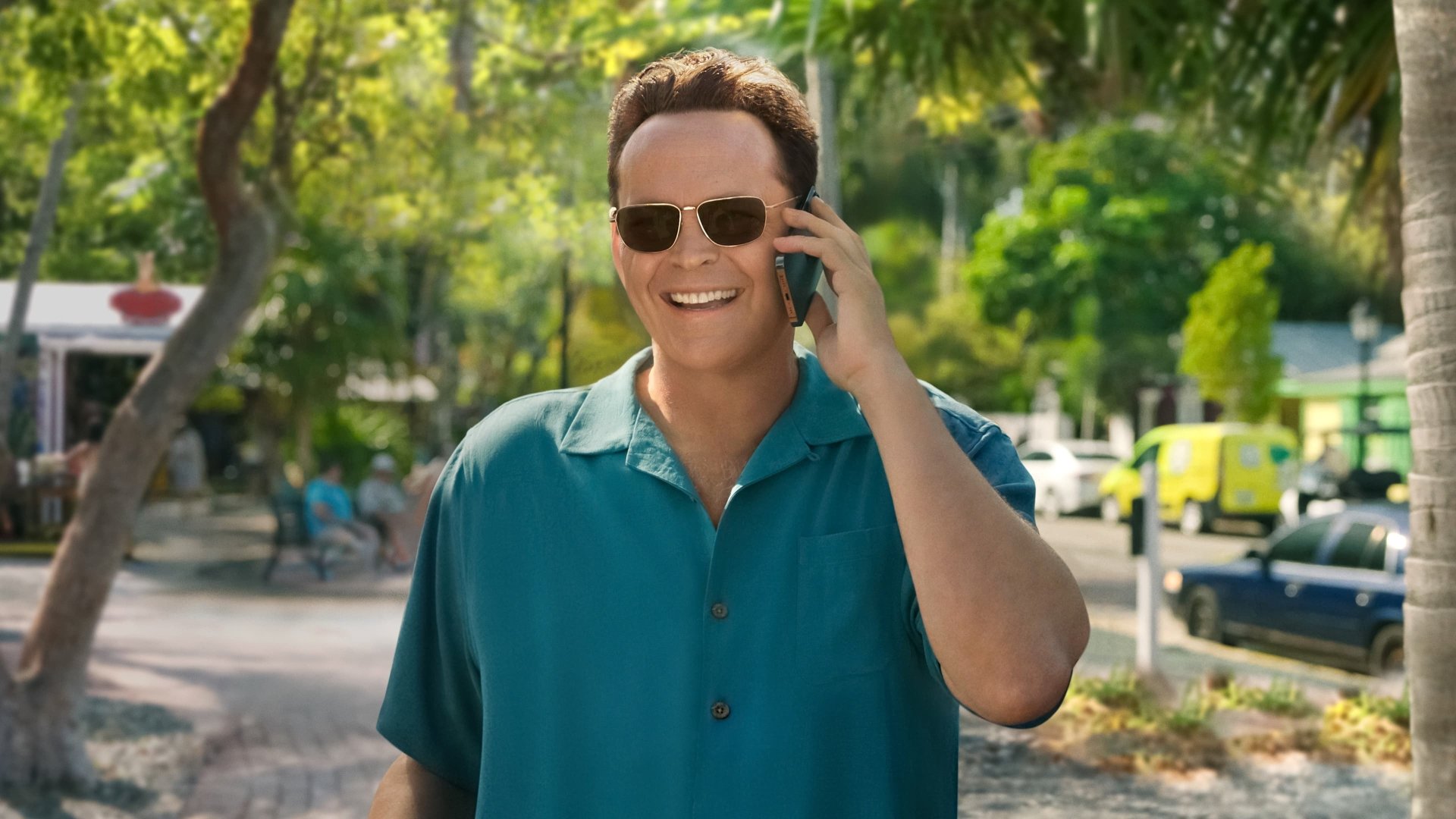 A vibrant HD wallpaper featuring Vince Vaughn in Bad Monkey, smiling and talking on the phone against a lush, green backdrop.