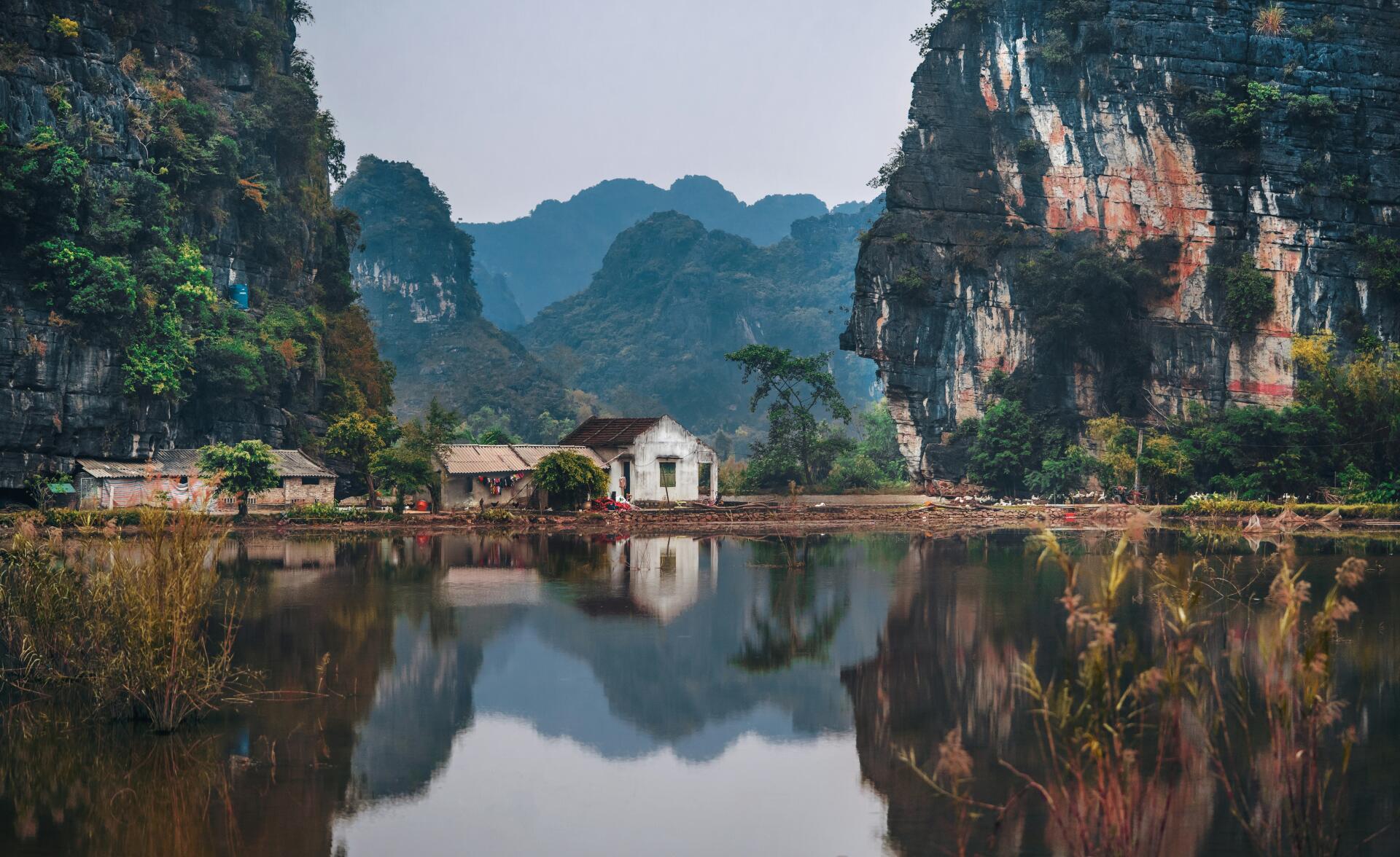 A serene Vietnamese village is reflected in the calm waters of a lake, surrounded by majestic mountains, creating a stunning landscape in vibrant 8K Ultra HD.