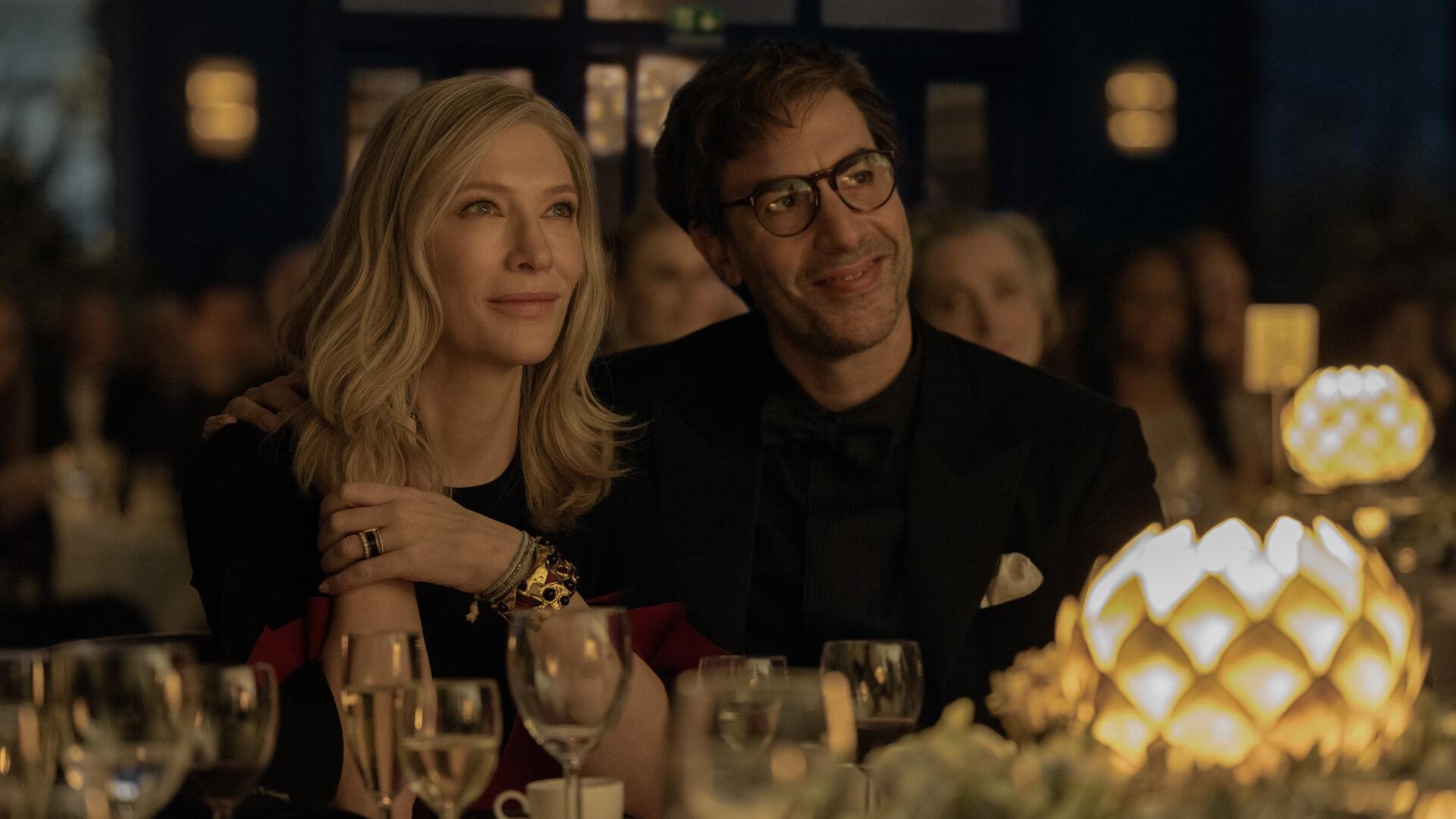 Cate Blanchett and Sacha Baron Cohen share a moment in a scene from the TV show **Disclaimer (2024)**, set against an elegant dinner backdrop with sparkling lights and glasses.