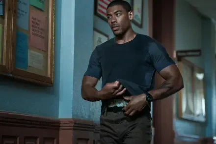 A scene from the movie Rebel Ridge features Aaron Pierre in a tense moment, set against a backdrop of muted colors and framed posters, captured in a stunning 4K Ultra HD wallpaper.