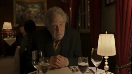 A dramatic scene from the TV show Disclaimer (2024) featuring Kevin Kline sitting at a restaurant table, with a soft-lit ambiance and wine glasses in view. 
