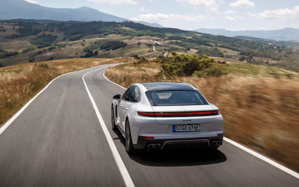 A sleek Porsche Panamera Turbo S E-Hybrid drives along a winding road, surrounded by rolling hills and a clear blue sky, creating a striking HD desktop wallpaper.