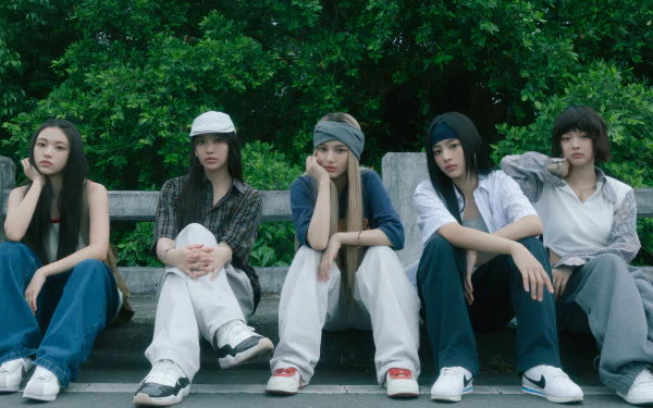 A stylish HD desktop wallpaper featuring the K-pop group NewJeans, showcasing five members sitting casually against a lush green background, embodying their unique aesthetic and music vibe.