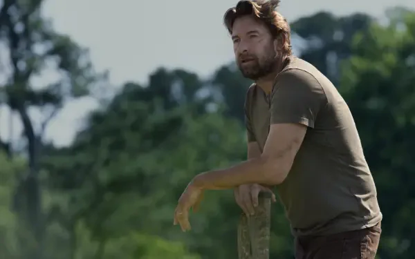 Scott Speedman gazes thoughtfully while leaning on a post in a lush, green landscape from the TV show Teacup (2024), captured in stunning 8K Ultra HD resolution.