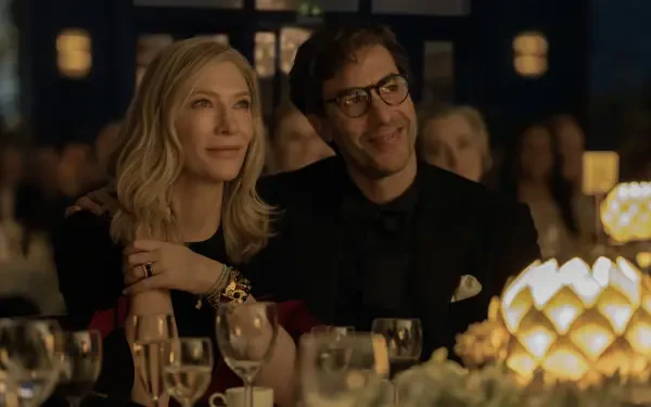 Cate Blanchett and Sacha Baron Cohen share a moment in a scene from the TV show **Disclaimer (2024)**, set against an elegant dinner backdrop with sparkling lights and glasses.