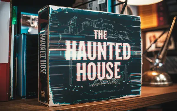 A stylish 4K Ultra HD PC Desktop wallpaper featuring a vintage game box titled The Haunted House, displayed on a wooden shelf with books and a lamp in a cozy setting.