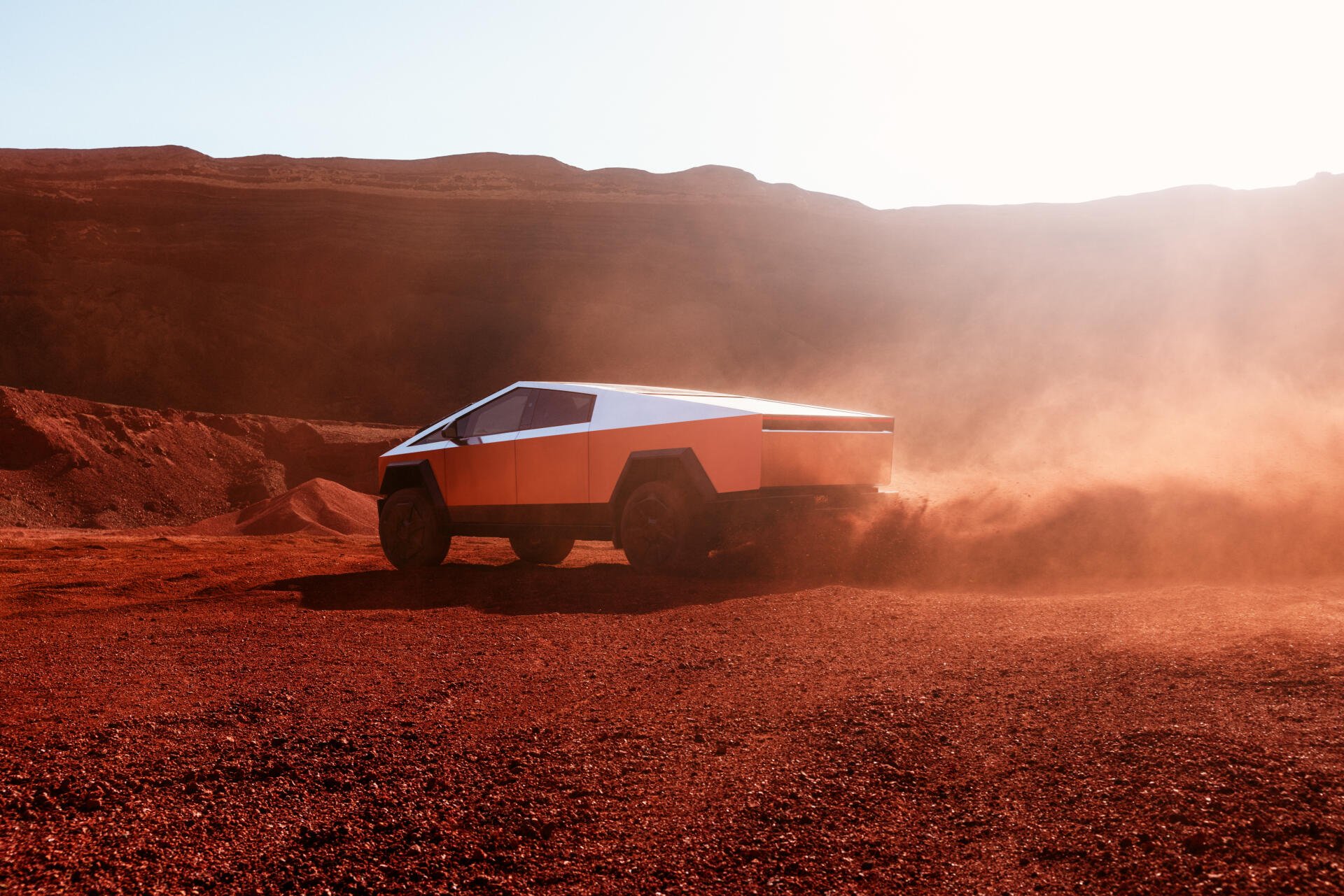 A Tesla Cybertruck maneuvers through rugged terrain, kicking up dust in a striking 4K Ultra HD backdrop, showcasing its futuristic design against a dramatic landscape.