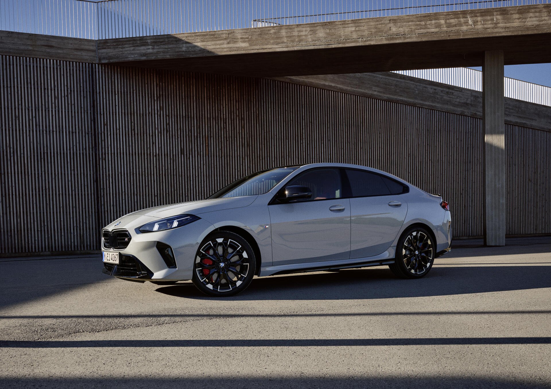A sleek silver BMW M235 Gran Coupe parked against a modern architectural backdrop, showcasing its stylish design and dynamic presence as an HD desktop wallpaper.
