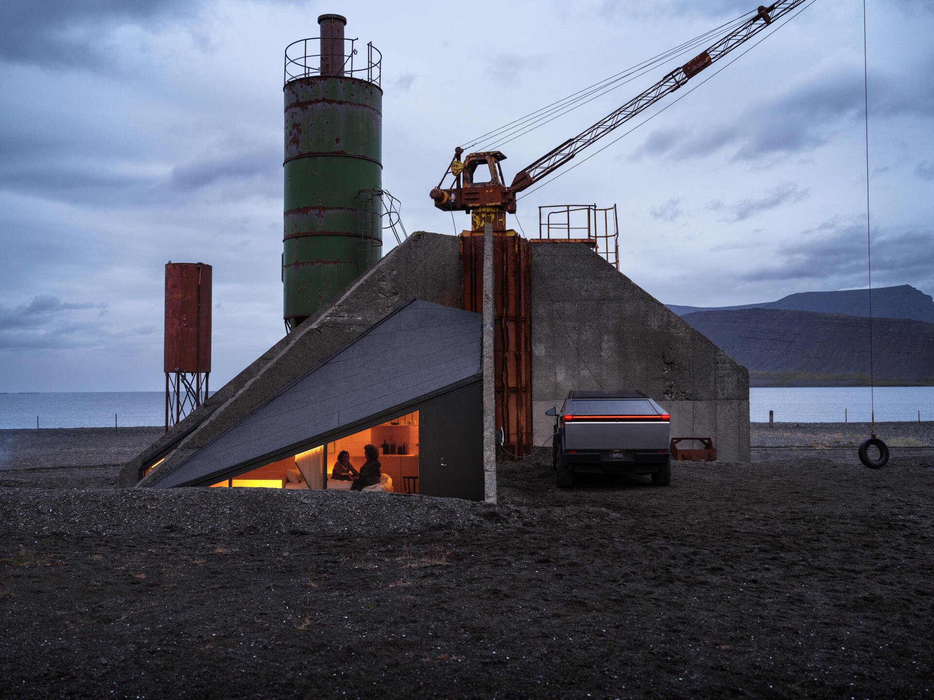 A Tesla Cybertruck is parked near a construction site at dusk, showcasing its modern design against an industrial backdrop. This 4K Ultra HD image captures a unique, atmospheric scene.