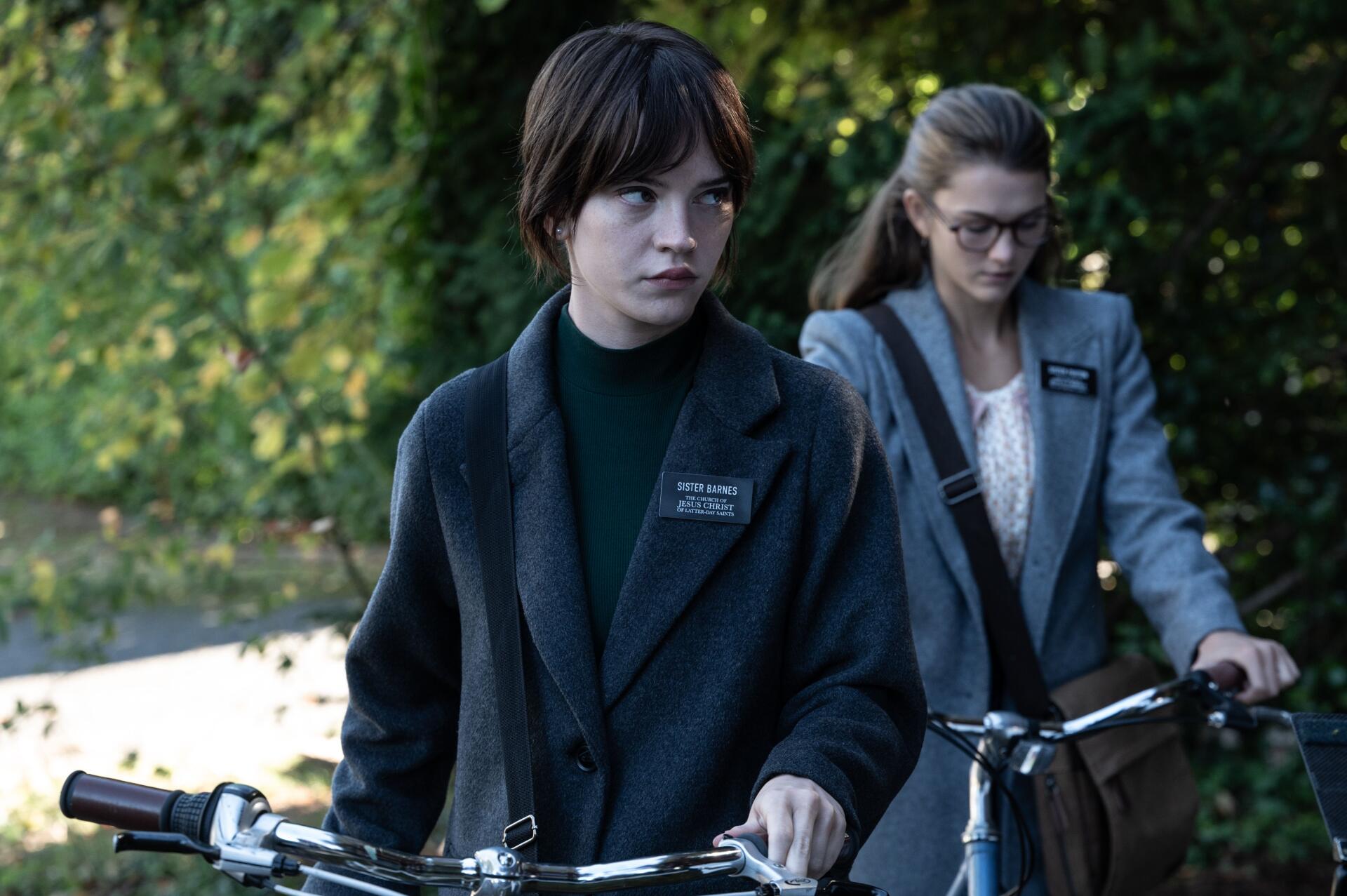 Sophie Thatcher in a scene from the 2024 movie Heretic, depicting two characters on bicycles amid a lush, green background, captured in stunning 4K Ultra HD.