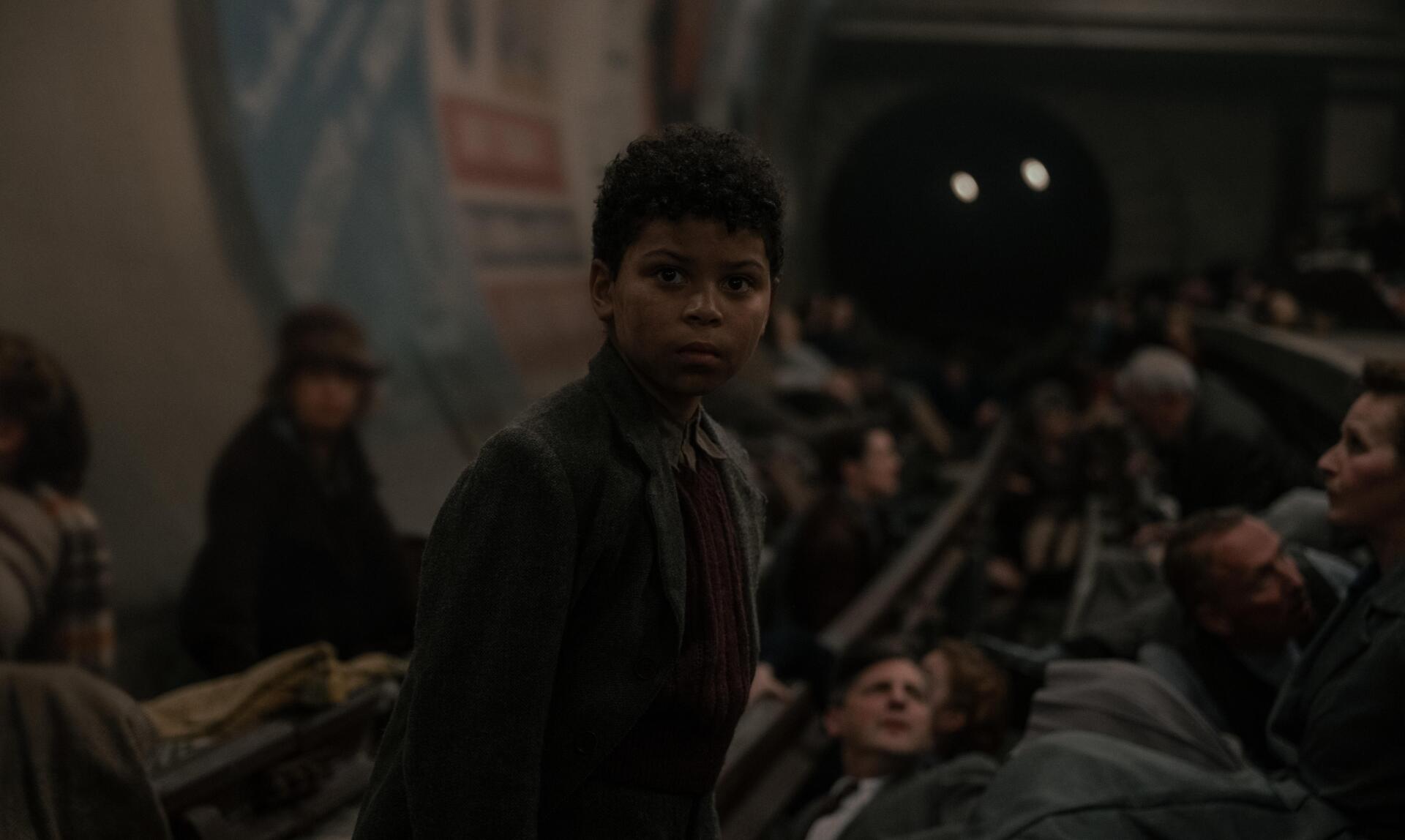A scene from the movie Blitz (2024) featuring Elliott Heffernan, showing a young character in a crowded underground setting, capturing a moment of tension and atmosphere. 