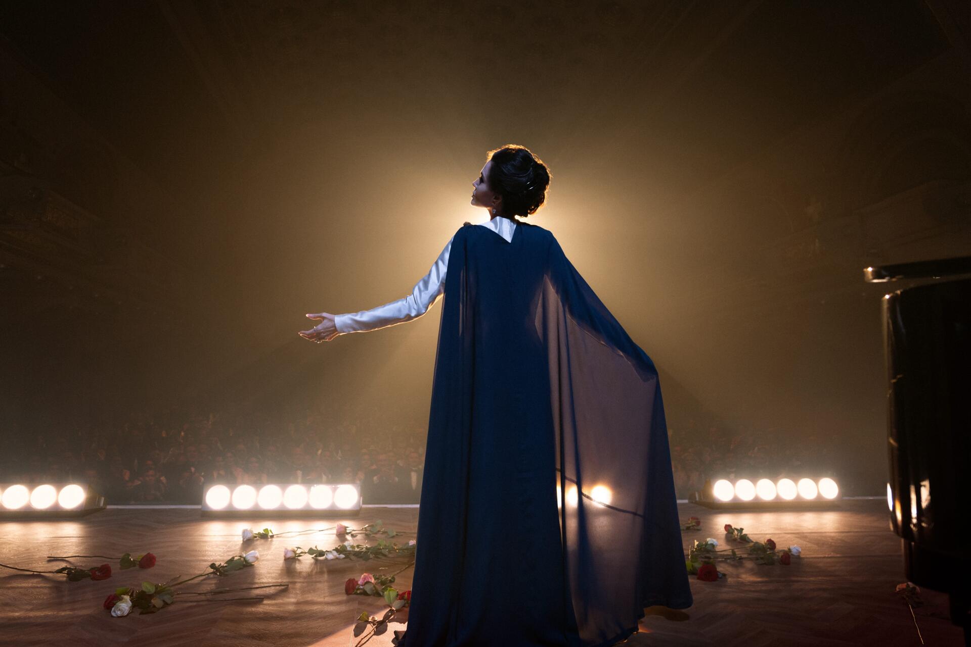 A stunning 4K Ultra HD wallpaper from the movie Maria (2024), featuring a performer in a flowing cape, standing in spotlight with rose petals scattered on stage.