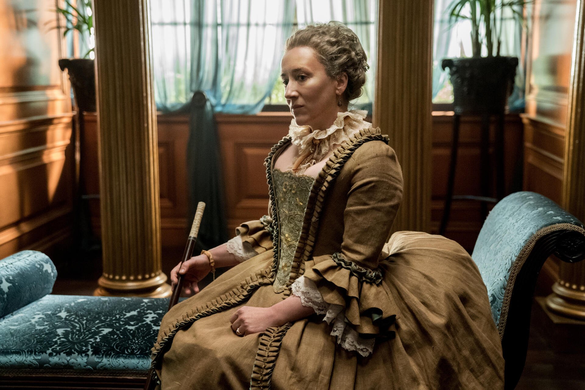 A character from the TV show Outlander, seated in a grand setting, wearing an elaborate vintage dress and poised with a quill, captured in rich detail for a 4K Ultra HD background.