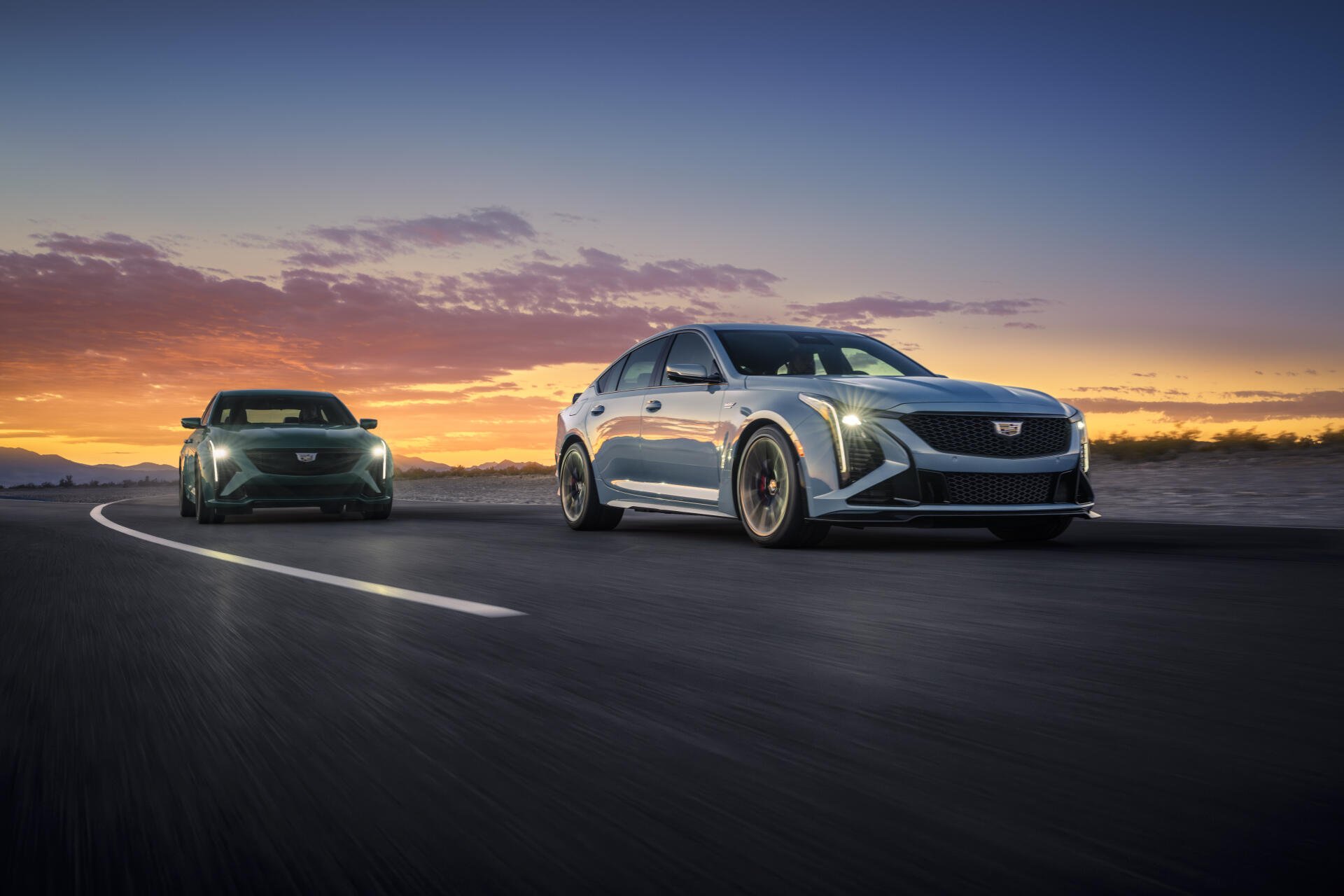 A stunning 8K Ultra HD desktop wallpaper featuring two Cadillac CT5-V Blackwing cars on a scenic road at sunset, highlighting their sleek design and powerful presence.