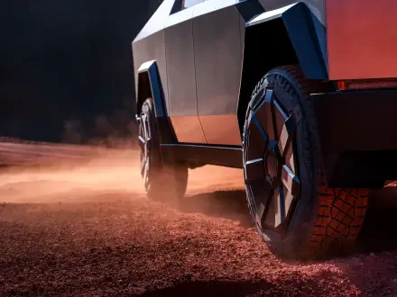 A close-up view of the Tesla Cybertruck's wheel on a rugged terrain, showcasing its distinctive design and tread against a backdrop of dust. 4K Ultra HD wallpaper.