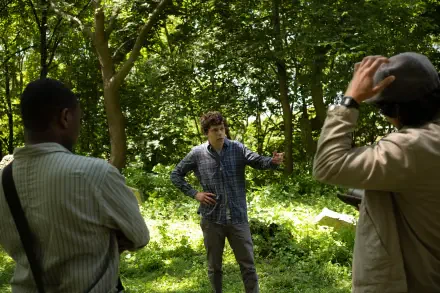 A scene from the movie A Real Pain, featuring Jesse Eisenberg engaged in conversation with two individuals in a lush, green forest setting. 4K Ultra HD desktop wallpaper.