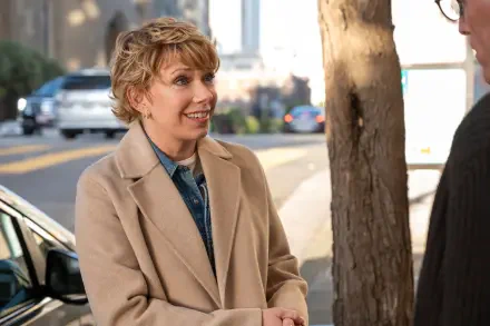 A scene from the TV show A Man on the Inside featuring Mary Elizabeth Ellis, smiling and engaging in conversation outdoors, framed by a tree and city backdrop.