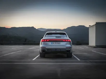 A sleek Audi RS Q8 parked in an empty lot, showcasing its modern design against a backdrop of mountains at sunset. A stunning 4K Ultra HD desktop wallpaper.