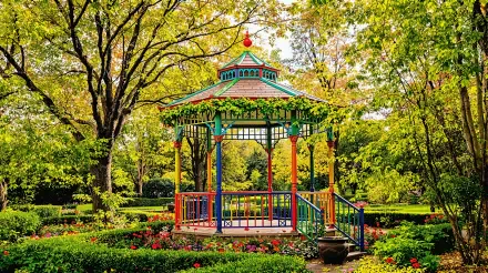 Colorful gazebo stands in a vibrant garden surrounded by lush greenery and blooming flowers, captured in a detailed 4K Ultra HD nature and architecture wallpaper.