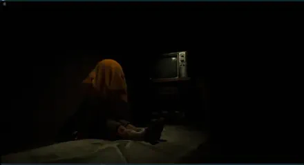 A dark scene from the video game The Cabin Factory, featuring a figure draped in a yellow cloth sitting by an old television, creating an eerie atmosphere for an HD PC wallpaper.