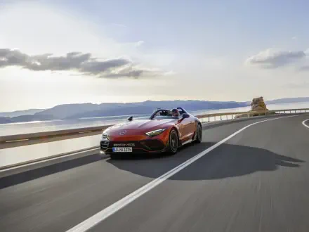 A sleek Mercedes-AMG PureSpeed sports car accelerates along a coastal road under a clear sky, showcasing its power and elegance in vibrant 4K Ultra HD resolution.